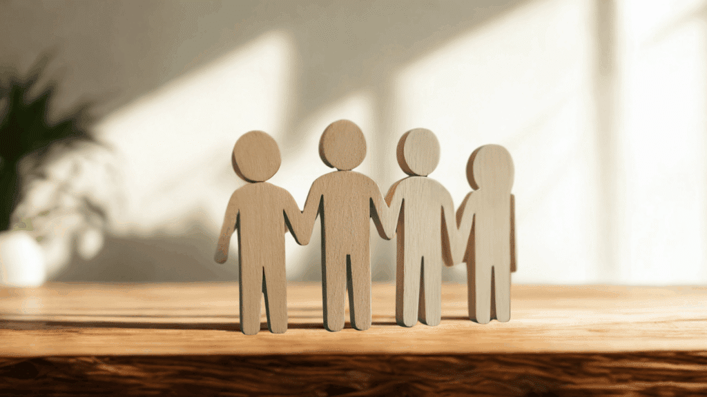 Four wooden human figures standing together holding hands on a table, symbolizing teamwork, unity, and collaboration
