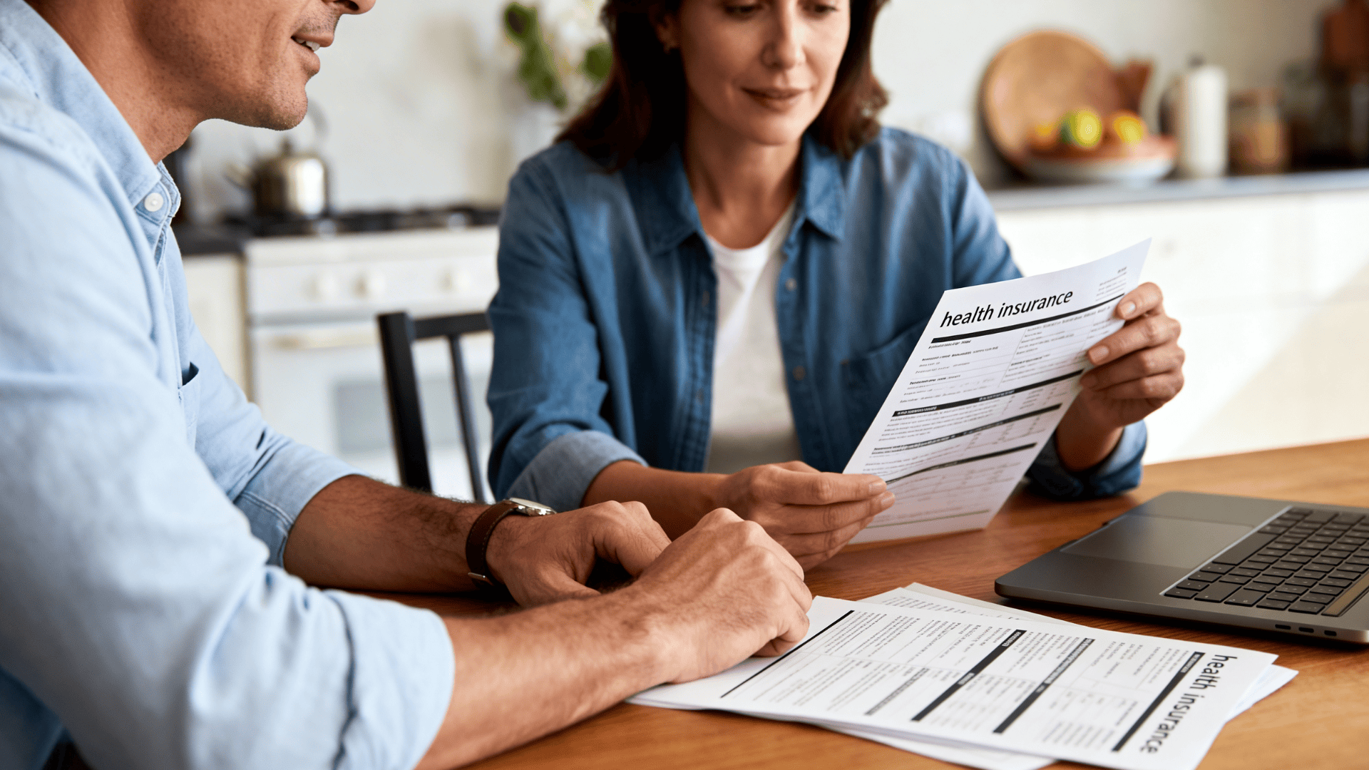 husband and wife reviewing health insurance paperwork and deductible information at a kitchen table.