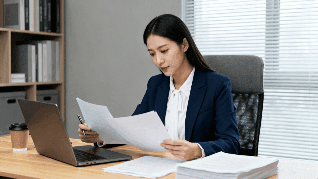 professional woman in an office reviewing a printed letter of support with a red pen while sitting at a desk with a laptop and papers (1)