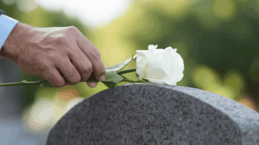 A person in a suit places a white rose on a headstone in a Bereavement Leave