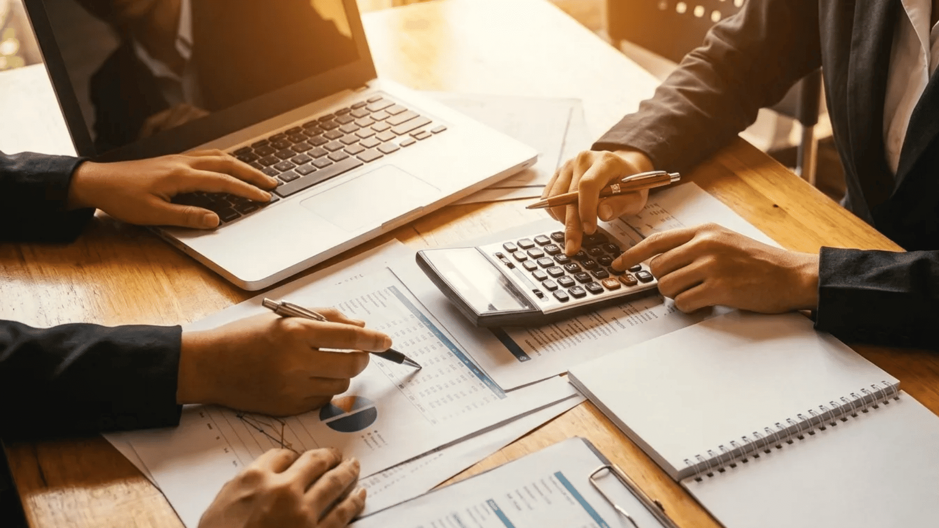 Corporate employees reviewing financial reports with a laptop and calculator during a business meeting.