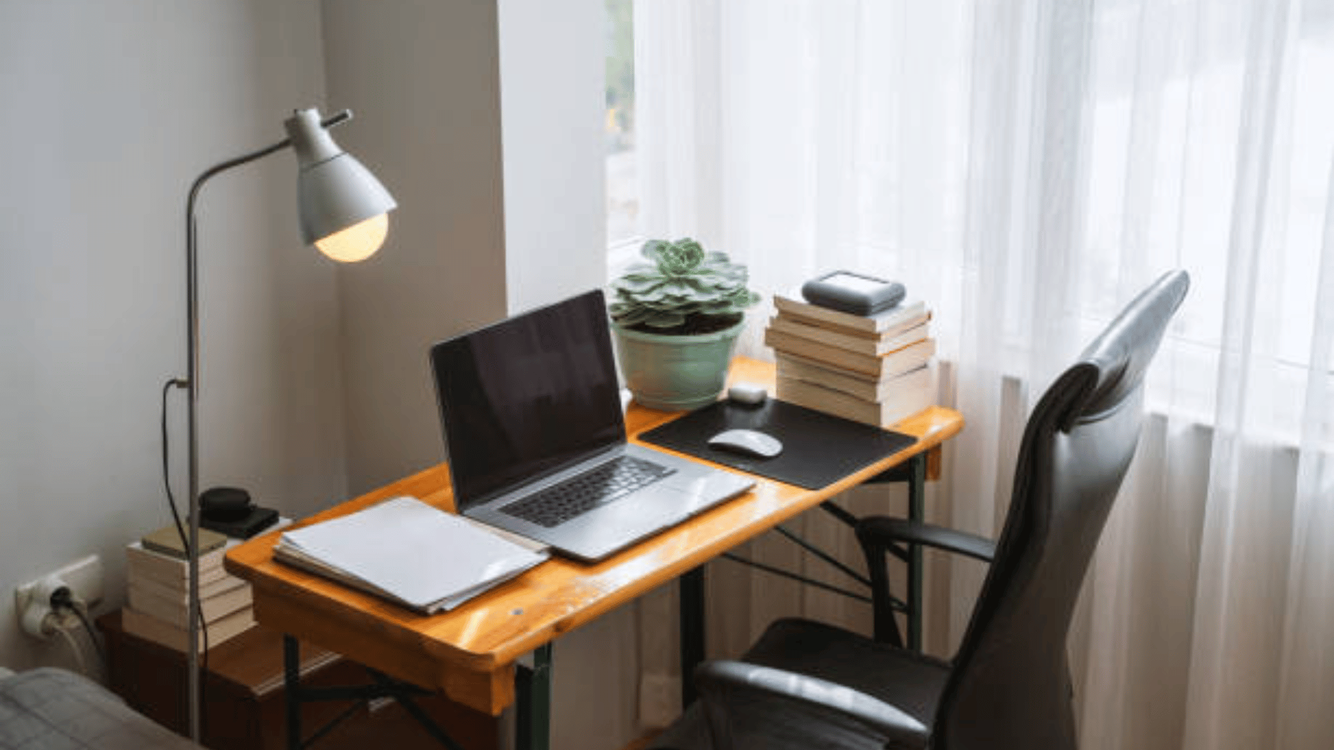 small table with laptop, lamp, and a stack of paper and books