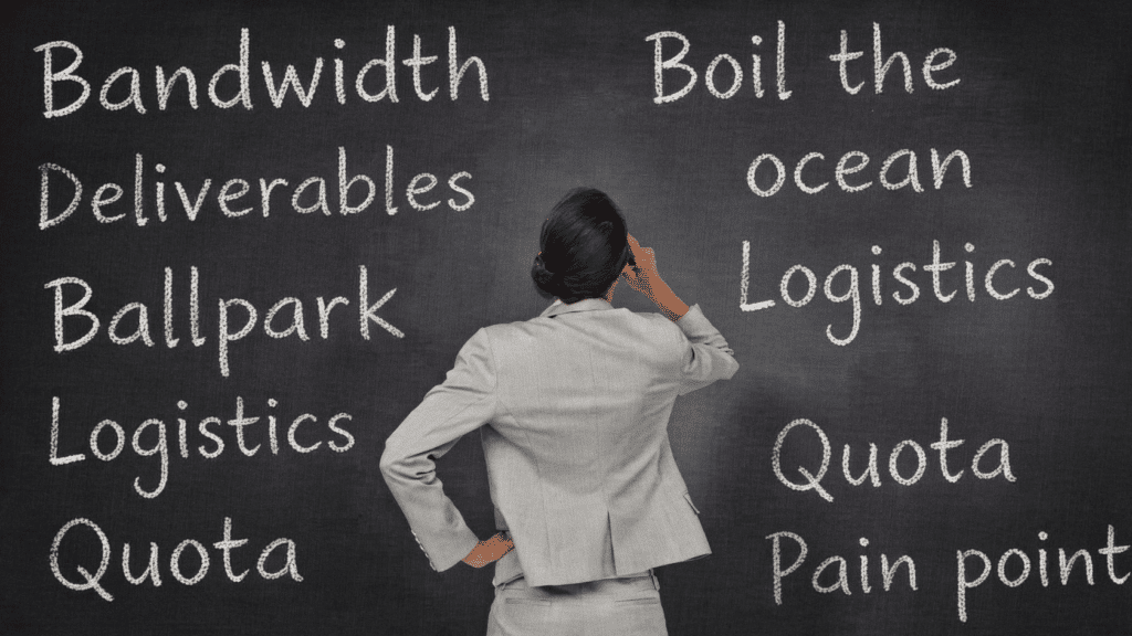 Businessperson facing a chalkboard filled with workplace buzzwords like bandwidth, deliverables, logistics, quota, and pain point.