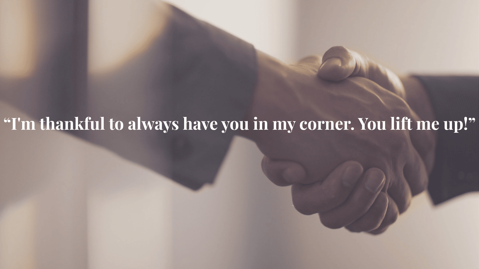 Close-up of two business professionals in suits sharing a firm handshake against a soft blurred background, representing partnership and agreement.