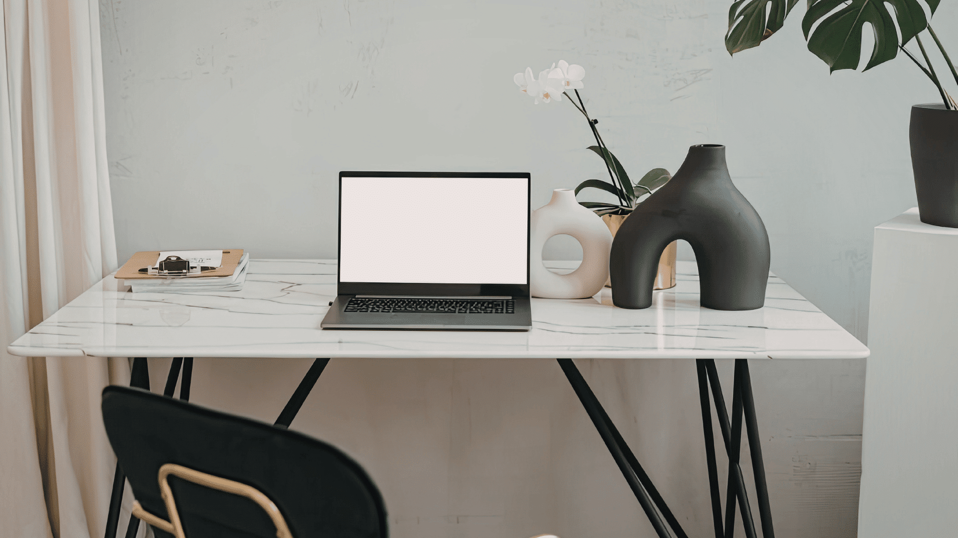 Minimal remote work setup with a laptop on a clean marble desk with plants