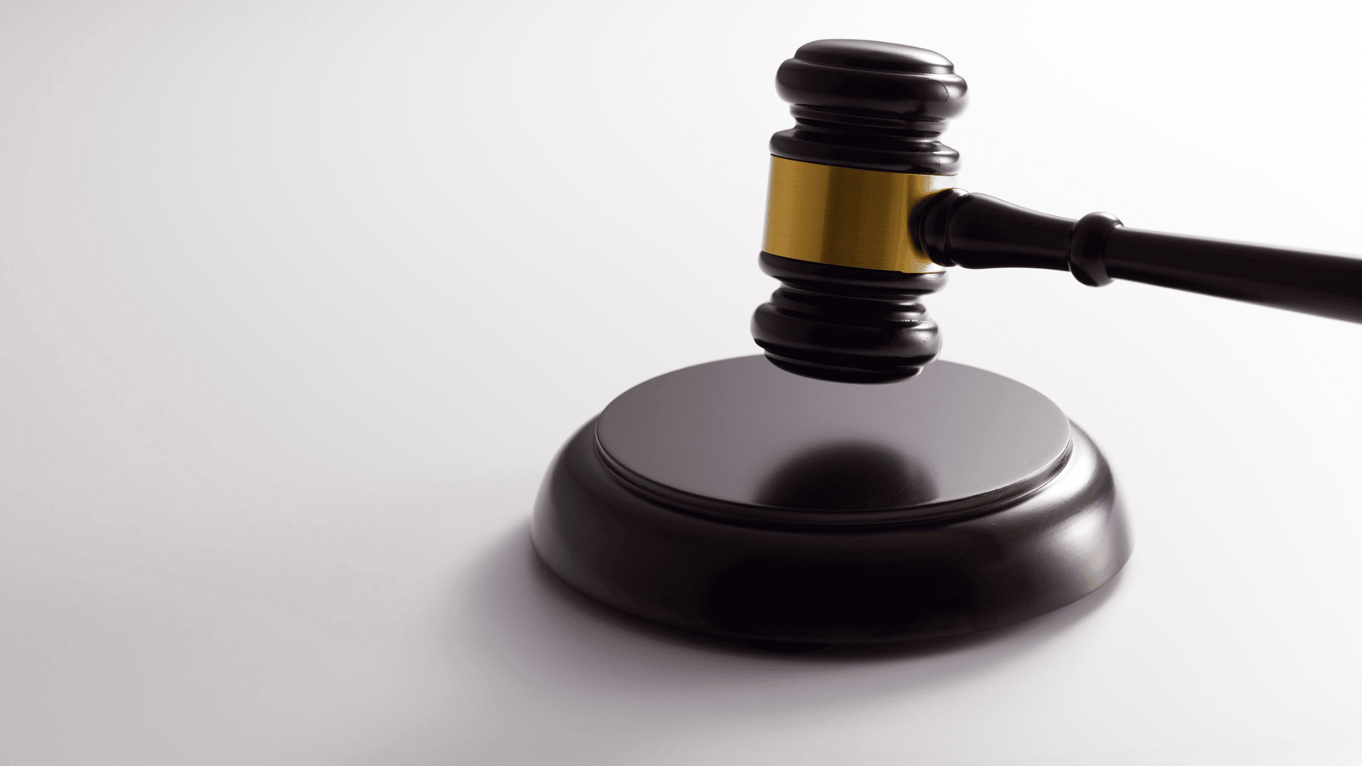 Black and gold gavel striking a sound block against a plain white background