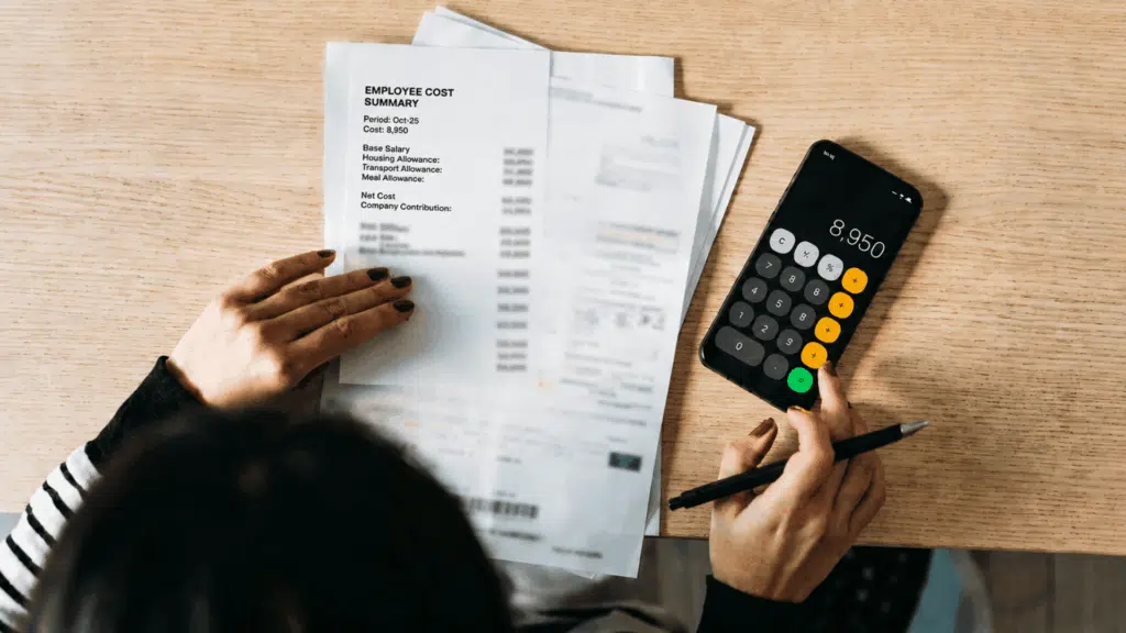 Overhead view of a desk showing a person using a smartphone calculator as an employee cost calculator.