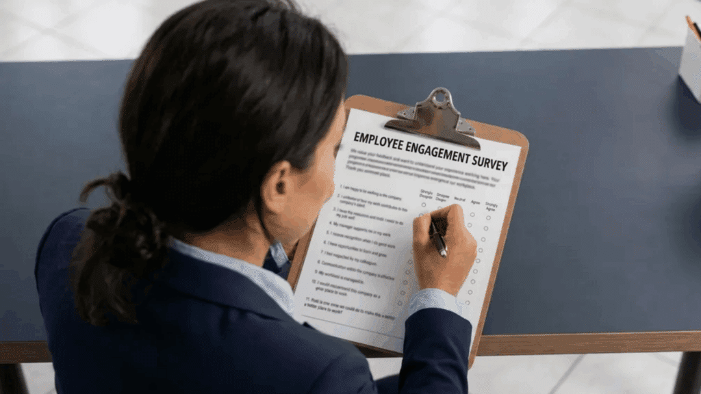 Person filling out an employee engagement survey on a clipboard at a desk.