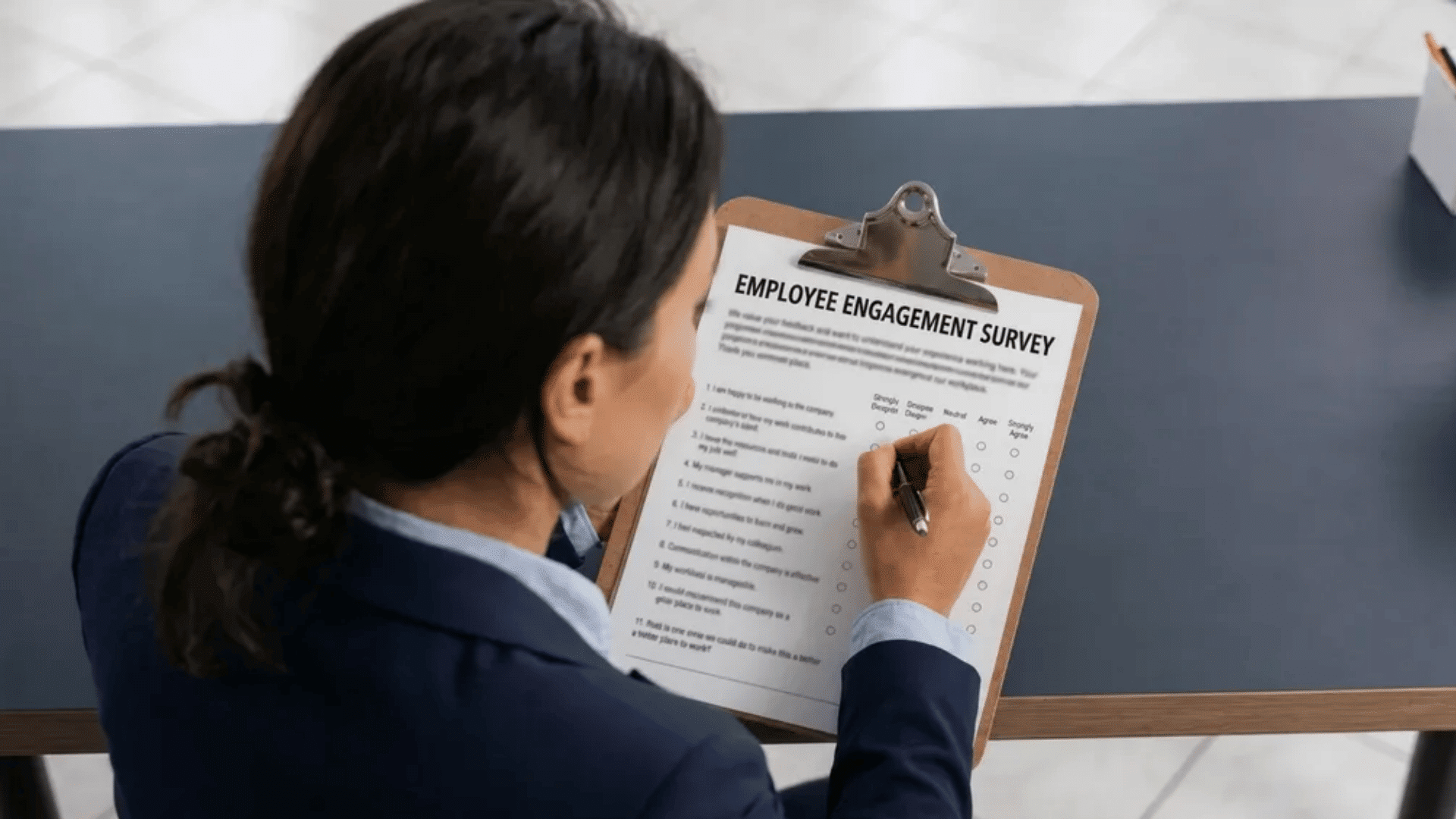 Person filling out an employee engagement survey on a clipboard at a desk.