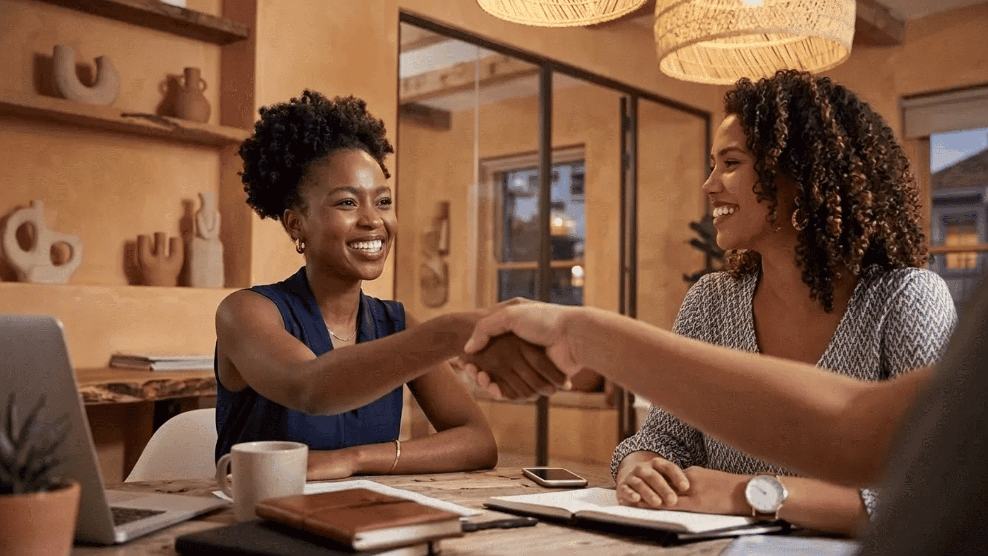 Two professionals shaking hands across a meeting table during a friendly business discussion in a modern office.