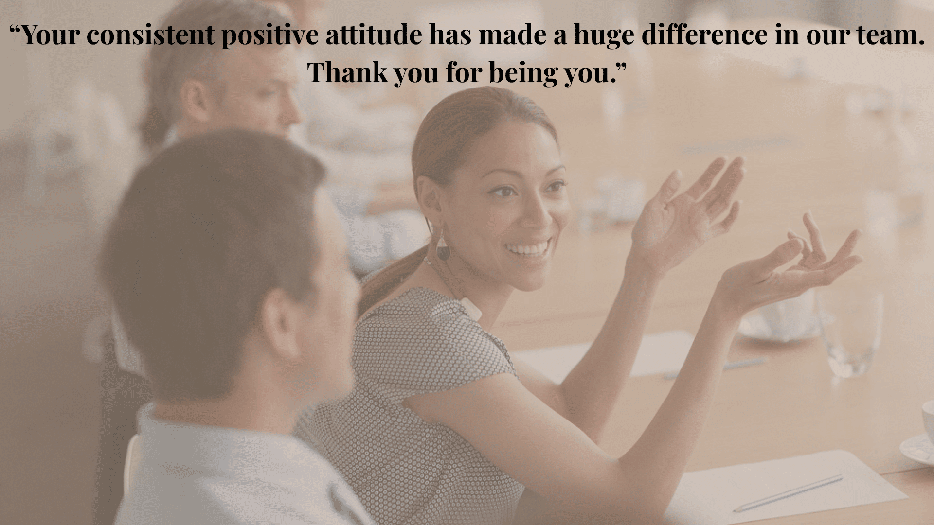 Smiling woman speaking and gesturing in a business meeting, with colleagues listening around a conference table.