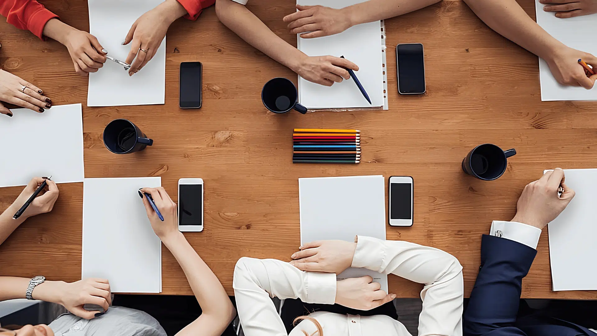 overhead view of a group meeting with papers, phones, and coffee cups on a wooden table