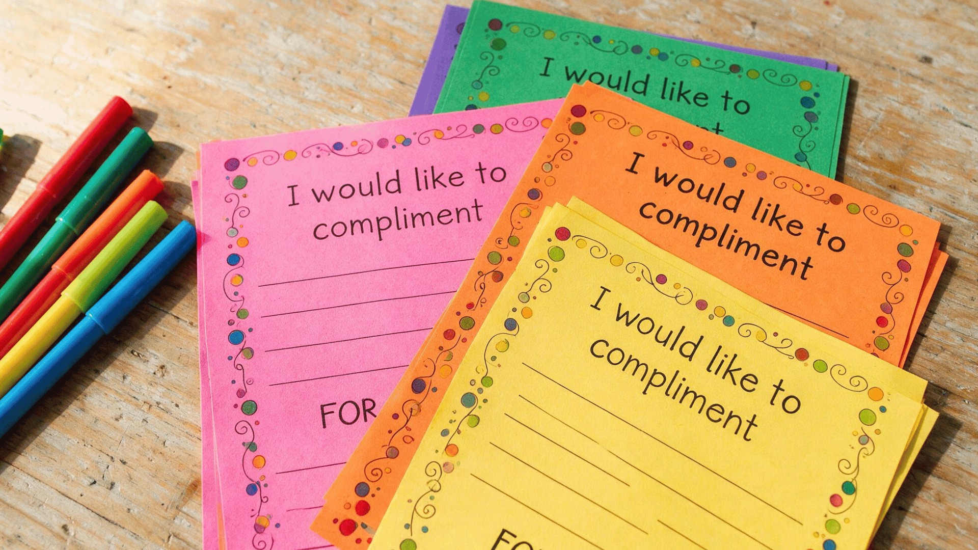 a stack of colorful paper compliment cards with blank lines sitting next to several bright color markers