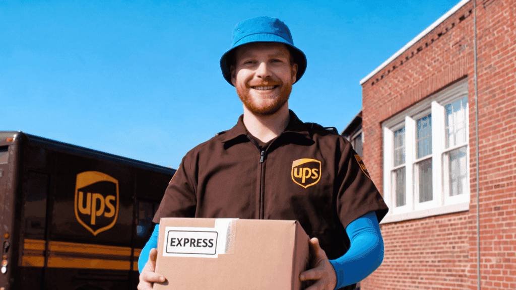 UPS delivery driver holding an express package by a delivery truck, representing UPS benefits and employee life.