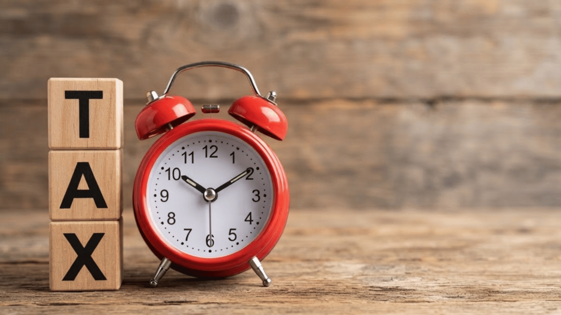 a red vintage alarm clock standing next to wooden blocks spelling tax on a rustic wooden table surface